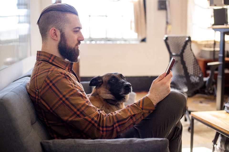 Man relaxing on a sofa at home with his dog, checking his phone